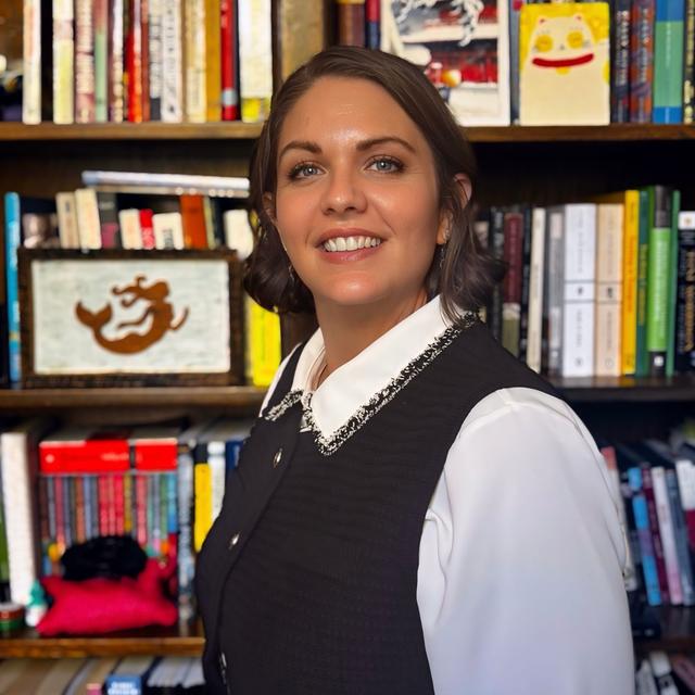 Lauren McKee portrait smiling with a dress shirt and vest and a background is a bookshelf.