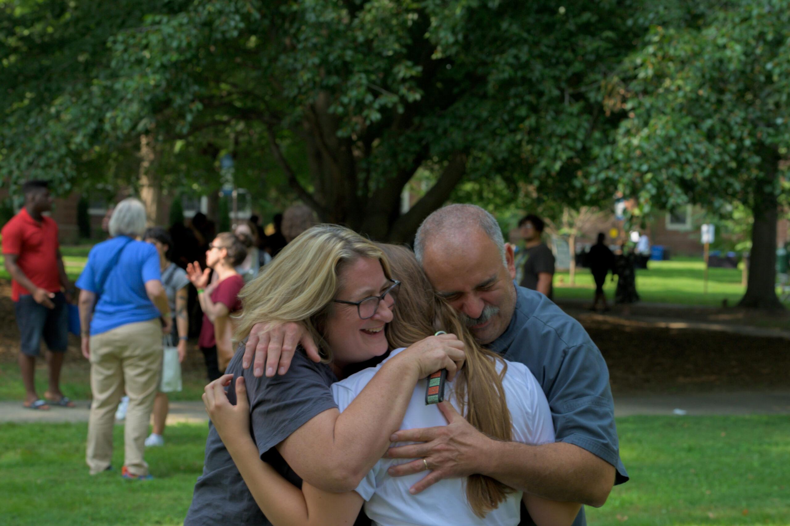 A photo of parents hugging their Berea student outside amongst green trees and grass.